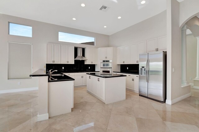 kitchen featuring wall chimney exhaust hood, decorative columns, white cabinets, and stainless steel appliances