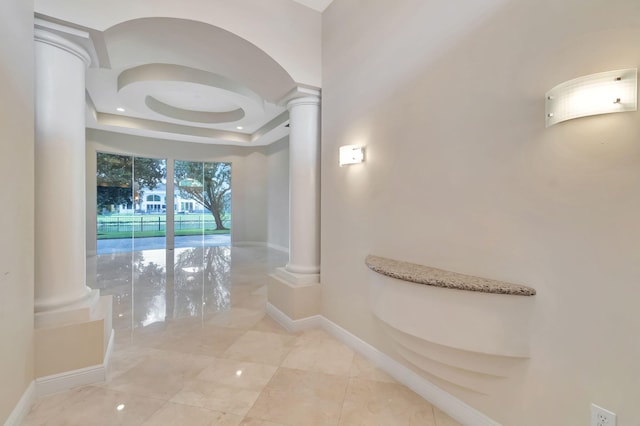 corridor with decorative columns and a raised ceiling