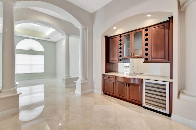 bar with light stone countertops, sink, beverage cooler, and ornate columns