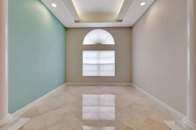 empty room featuring a raised ceiling and decorative columns