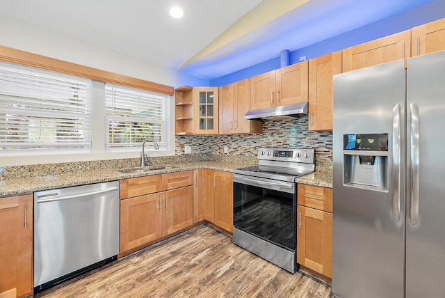 kitchen with lofted ceiling, sink, appliances with stainless steel finishes, light stone counters, and light hardwood / wood-style floors