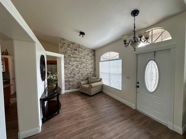 entrance foyer featuring dark wood-type flooring, vaulted ceiling, a notable chandelier, and a textured ceiling