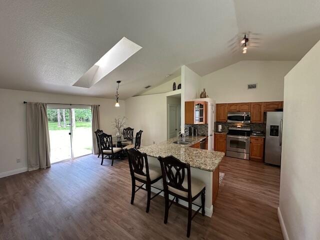 kitchen with a kitchen bar, kitchen peninsula, stainless steel appliances, lofted ceiling with skylight, and dark hardwood / wood-style floors