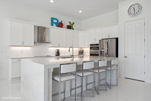 kitchen with white cabinetry, a kitchen island with sink, stainless steel appliances, and wall chimney exhaust hood