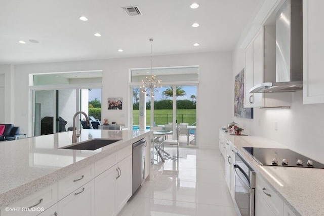 kitchen featuring wall chimney range hood, sink, appliances with stainless steel finishes, white cabinetry, and hanging light fixtures