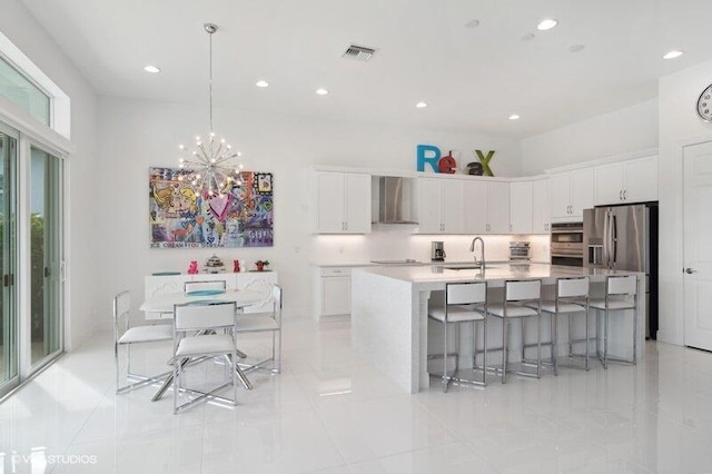 kitchen featuring white cabinets, sink, a center island with sink, and wall chimney range hood