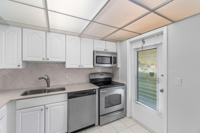 kitchen with stainless steel appliances, sink, light tile patterned floors, white cabinetry, and tasteful backsplash