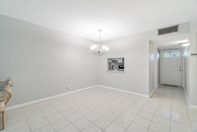 spare room with a notable chandelier, a textured ceiling, and light tile patterned floors