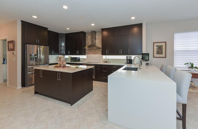 kitchen with a breakfast bar area, wall chimney exhaust hood, kitchen peninsula, stainless steel fridge, and sink