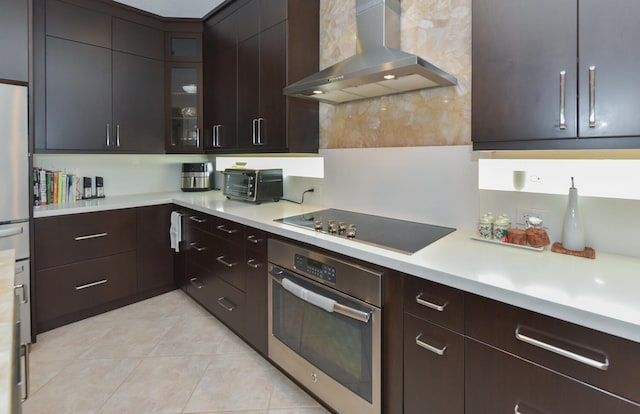 kitchen with black electric cooktop, wall chimney exhaust hood, oven, dark brown cabinets, and light tile patterned floors