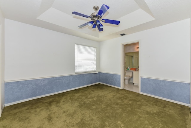 unfurnished room featuring ceiling fan, a tray ceiling, and dark carpet