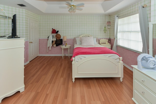 bedroom with ceiling fan, light wood-type flooring, and a raised ceiling