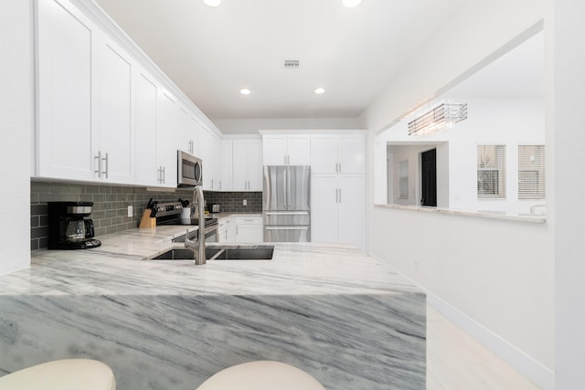 kitchen featuring a sink, stainless steel appliances, white cabinets, decorative backsplash, and light stone countertops