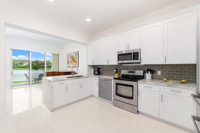 kitchen with a peninsula, a sink, decorative backsplash, appliances with stainless steel finishes, and white cabinetry