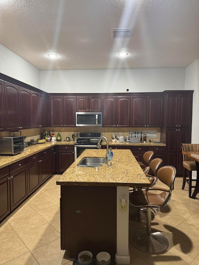 kitchen featuring backsplash, a breakfast bar, stainless steel appliances, sink, and a center island with sink