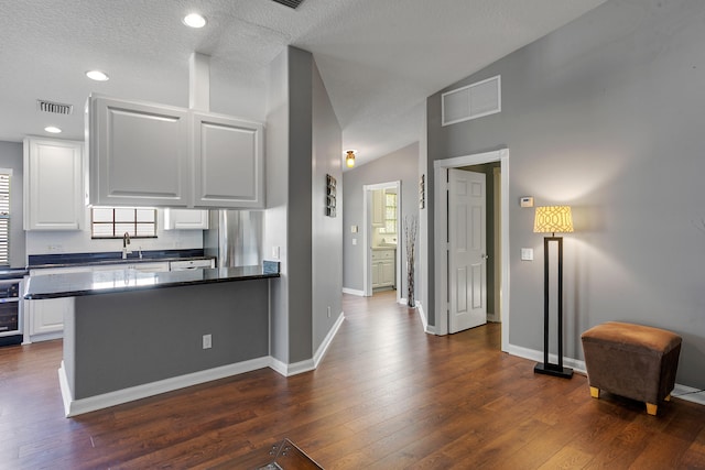 kitchen with a textured ceiling, dark hardwood / wood-style flooring, kitchen peninsula, white cabinetry, and vaulted ceiling