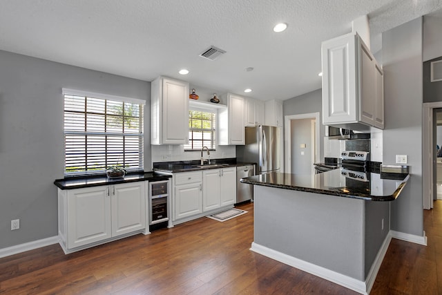 kitchen featuring white cabinets, kitchen peninsula, stainless steel appliances, and dark hardwood / wood-style flooring