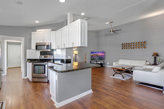 kitchen with lofted ceiling, dark wood-type flooring, stainless steel appliances, white cabinetry, and ceiling fan