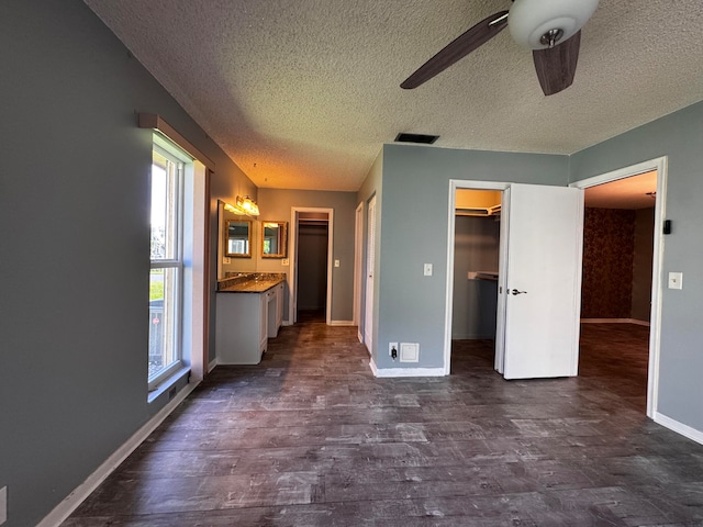 unfurnished bedroom with connected bathroom, dark hardwood / wood-style floors, a walk in closet, a textured ceiling, and ceiling fan