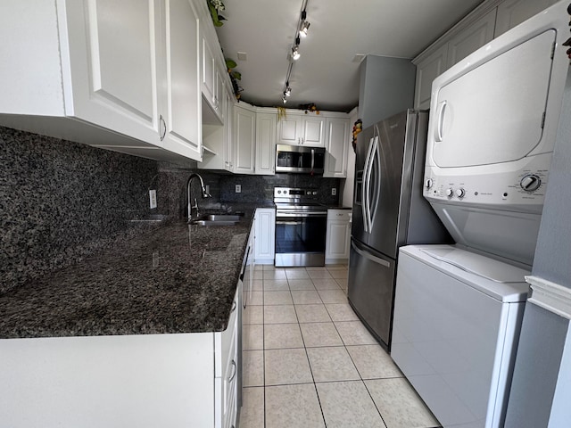 kitchen featuring appliances with stainless steel finishes, white cabinets, stacked washer and clothes dryer, and sink