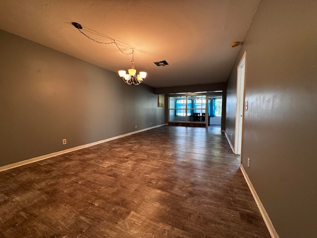 spare room featuring an inviting chandelier and dark wood-type flooring