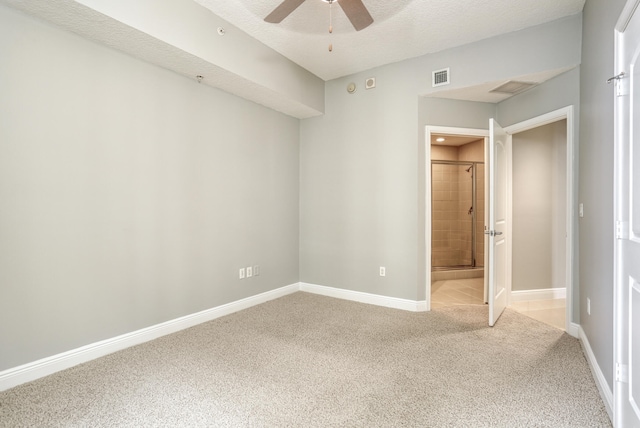 unfurnished bedroom featuring light carpet, a textured ceiling, ensuite bathroom, and ceiling fan