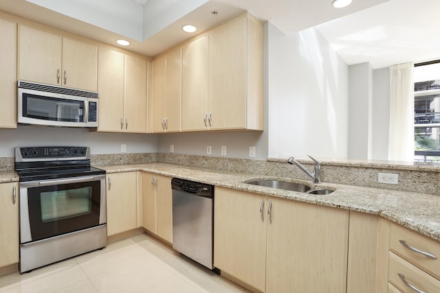 kitchen with appliances with stainless steel finishes, light stone countertops, sink, and light brown cabinetry