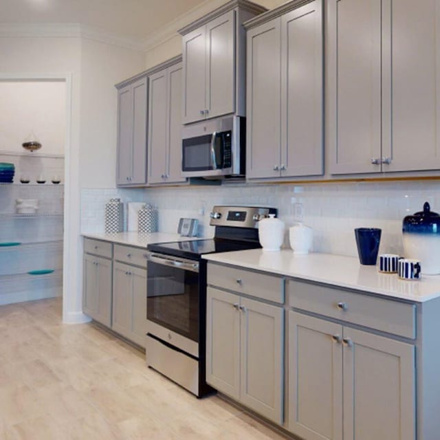 kitchen featuring gray cabinetry, stainless steel appliances, decorative backsplash, and ornamental molding