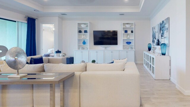 living room featuring light hardwood / wood-style floors, a raised ceiling, and ornamental molding