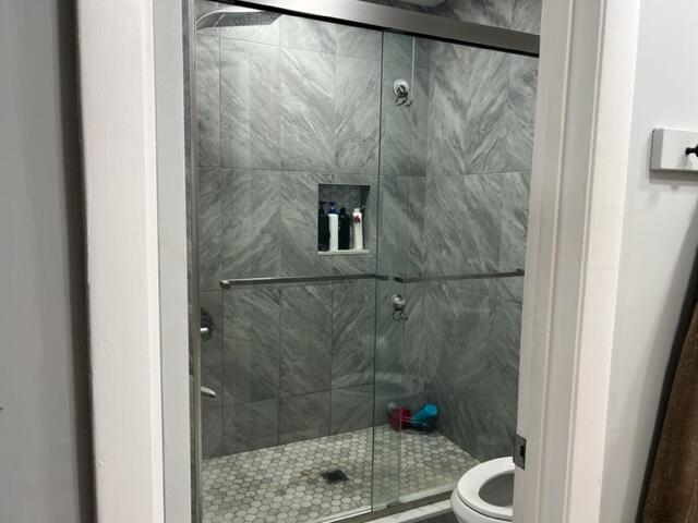 bathroom with a shower with shower door and toilet