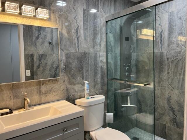 bathroom featuring toilet, vanity, tile walls, and a shower with door