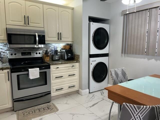 kitchen featuring backsplash, appliances with stainless steel finishes, ceiling fan, stacked washer and dryer, and cream cabinetry