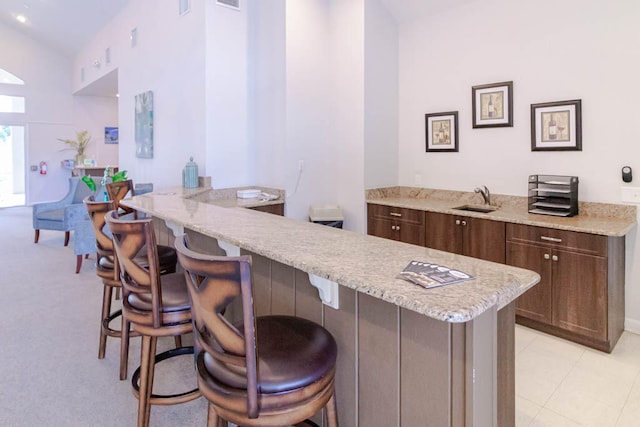 bar featuring light stone counters, dark brown cabinets, vaulted ceiling, sink, and light tile patterned floors