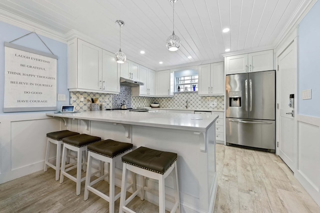 kitchen featuring white cabinets, under cabinet range hood, light wood-type flooring, a peninsula, and stainless steel fridge