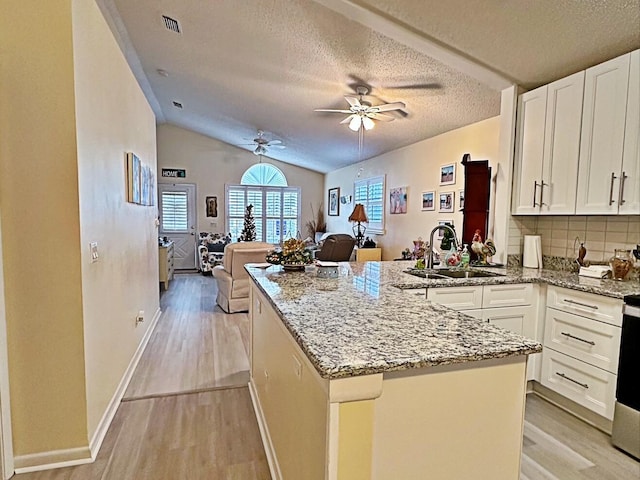 kitchen with white cabinetry, sink, light stone countertops, vaulted ceiling, and a textured ceiling