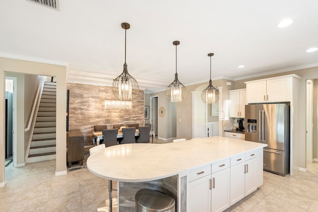 kitchen with a center island, hanging light fixtures, high end refrigerator, white cabinets, and ornamental molding