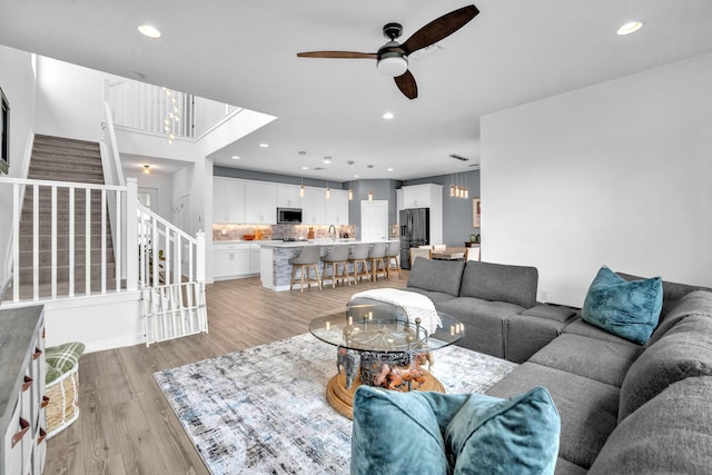 living room with stairs, ceiling fan, light wood-type flooring, and recessed lighting