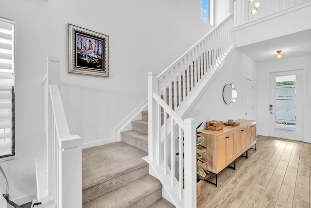 stairs with a high ceiling, wood finished floors, and baseboards