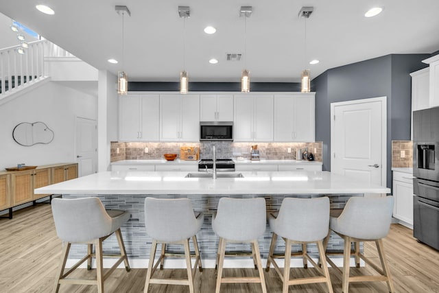 kitchen featuring decorative light fixtures, stainless steel appliances, visible vents, light countertops, and a center island with sink