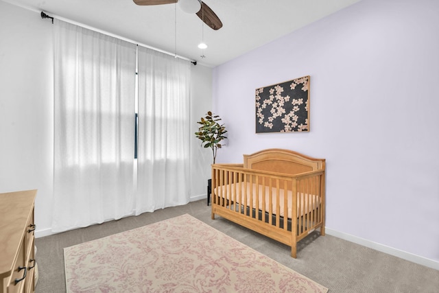 carpeted bedroom with ceiling fan, a crib, and baseboards