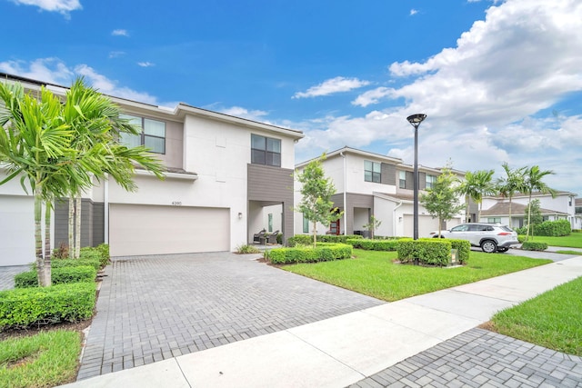 multi unit property featuring a garage, decorative driveway, a residential view, stucco siding, and a front yard