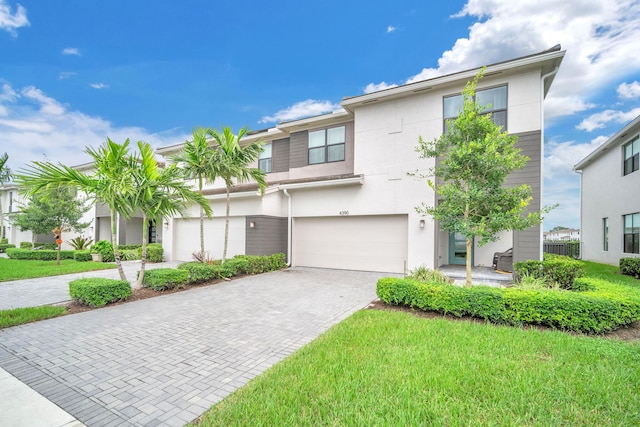 view of front of home featuring a garage, decorative driveway, a front lawn, and stucco siding