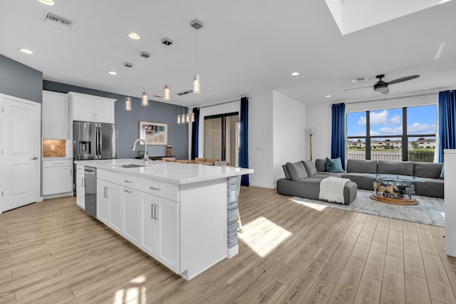 kitchen featuring a center island with sink, white cabinets, open floor plan, light countertops, and a sink