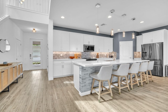 kitchen featuring white cabinets, appliances with stainless steel finishes, light countertops, and hanging light fixtures