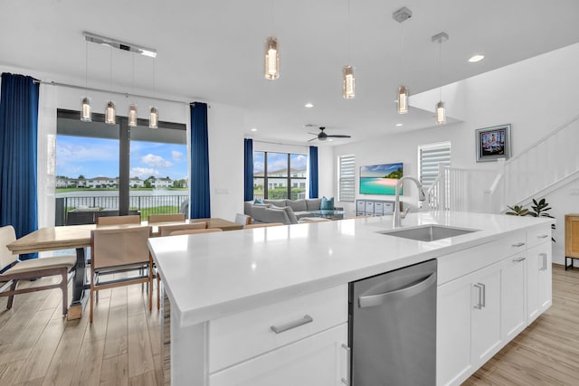 kitchen with decorative light fixtures, open floor plan, a kitchen island with sink, a sink, and dishwasher