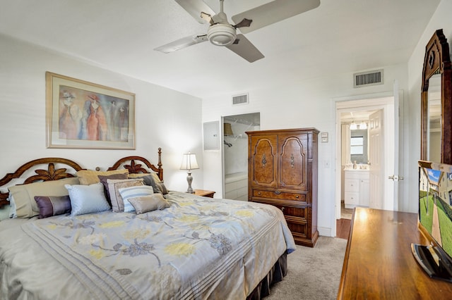 bedroom with ensuite bathroom, light colored carpet, and ceiling fan