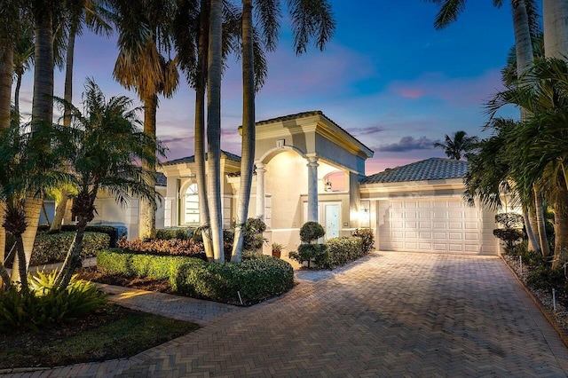 mediterranean / spanish-style house with a garage, stucco siding, and decorative driveway