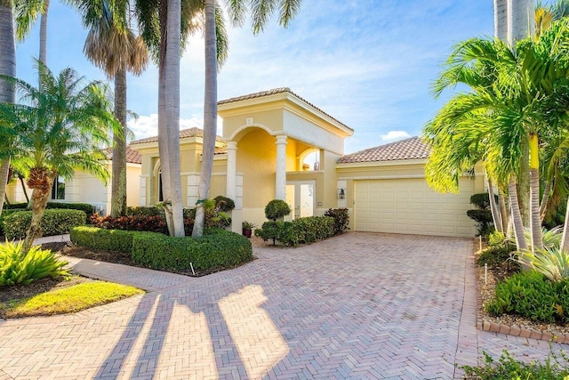 mediterranean / spanish-style house with a tile roof, an attached garage, stucco siding, and decorative driveway