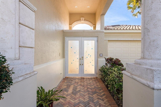 view of exterior entry with stucco siding, french doors, and an attached garage