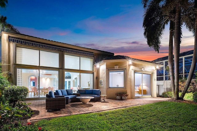 back house at dusk featuring a patio, outdoor lounge area, and a lawn